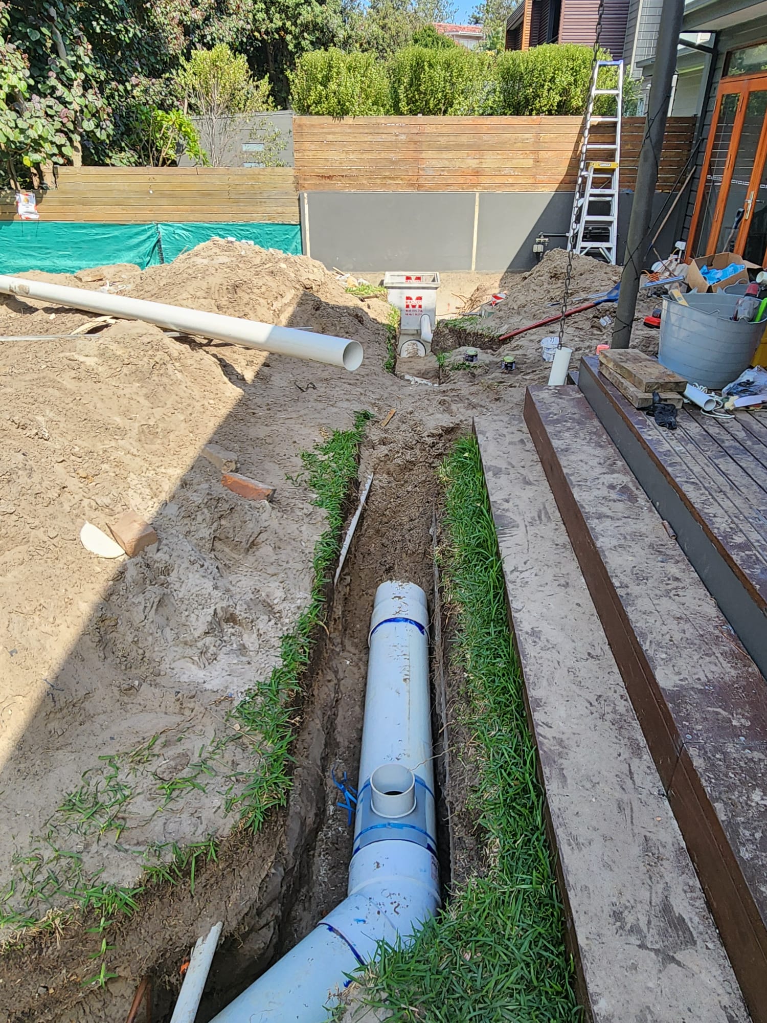New PVC sewer line laid in a trench through a backyard, with a pit and fresh pipe in the background