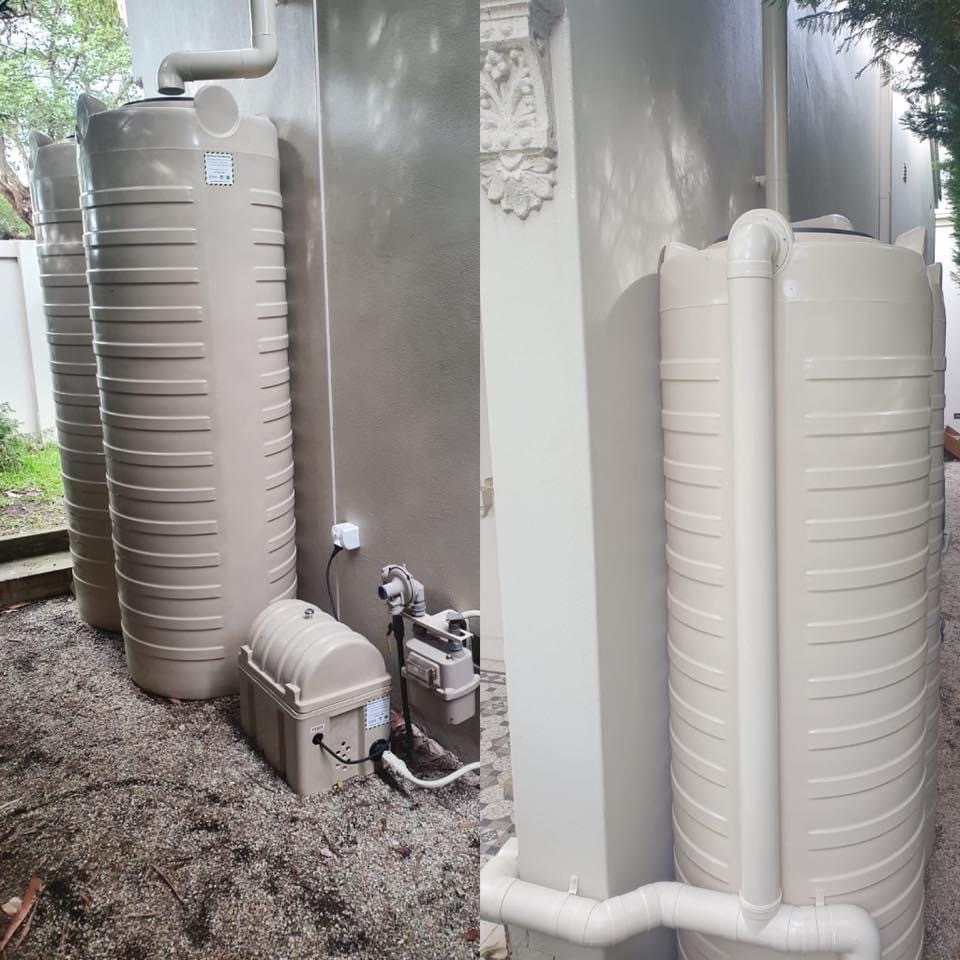 Two slimline rainwater tanks with a pump installed against a rendered wall