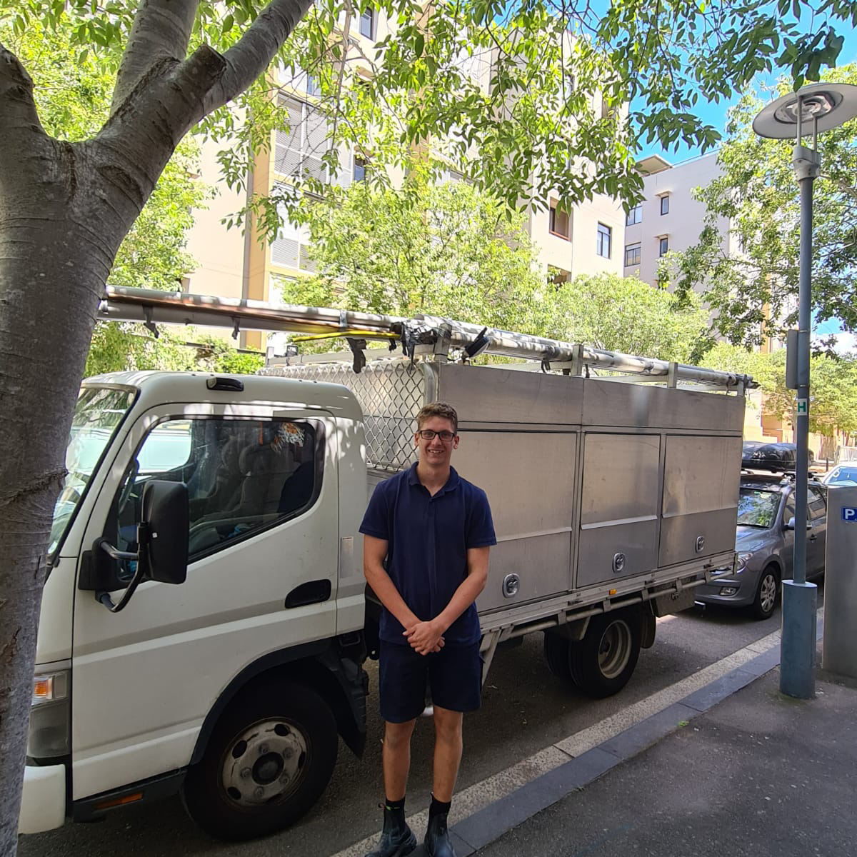 A PKG Plumbing team member in a navy polo standing in front of the white PKG work truck