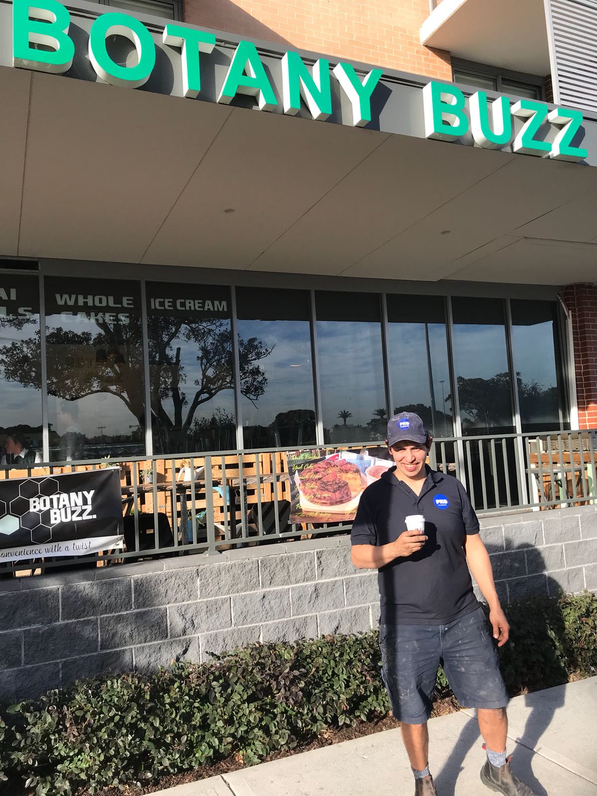 A PKG plumber in a branded cap and polo with a coffee outside a local cafe in Botany